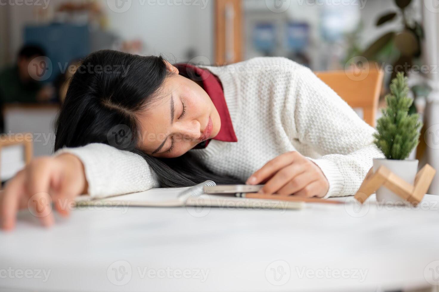 An asian woman is looking bored or sleepy while looking through her phone, Sitting at the cafe table photo