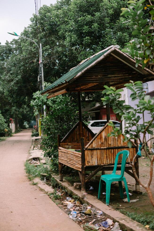 Rustic bamboo structure with green roof and a plastic chair by the roadside photo