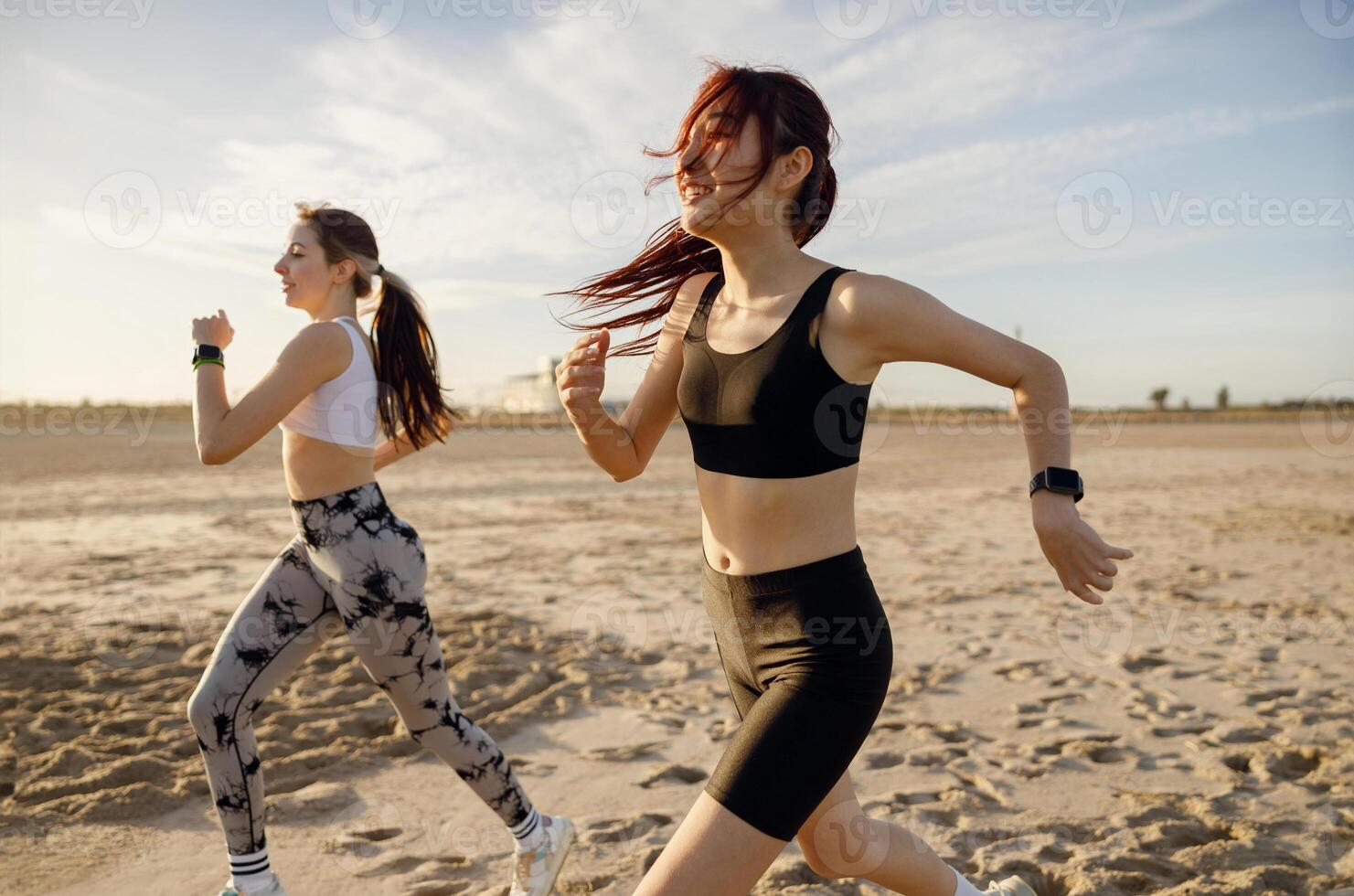 Young female friends in sportswear running on beach in morning sunrise. Outdoor workout routine photo