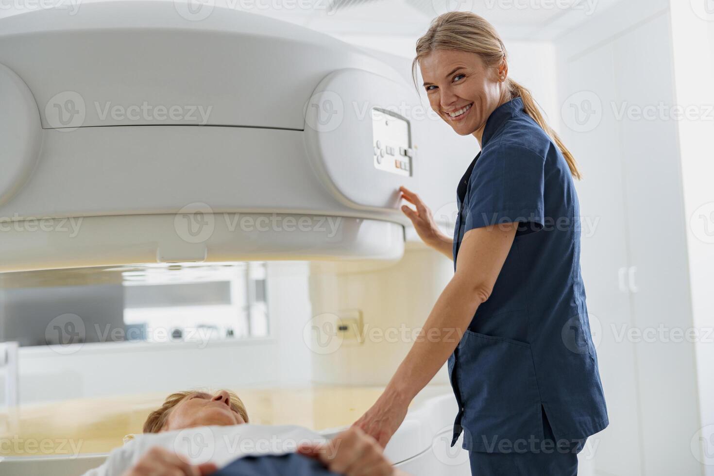 Radiologist controls MRI or CT or PET Scan with patient undergoing procedure and looking camera photo