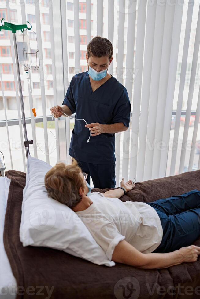 Doctor putting a drip on the arm of her patient in mask during pandemic of Covid 19 photo