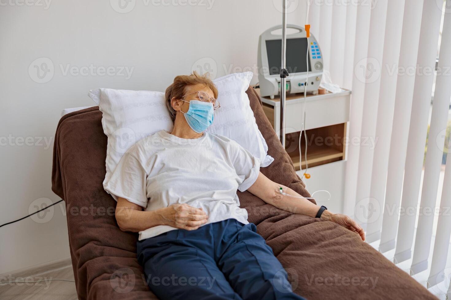 Sick woman attached to an intravenous drip lying on bed in a hospital ward photo