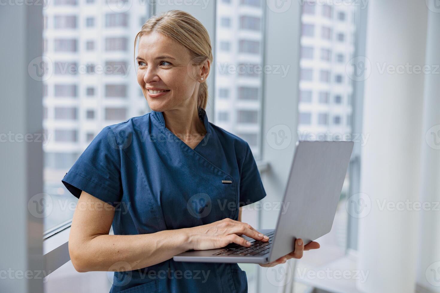 Female healthcare worker using laptop while working at doctor's office and looking window photo