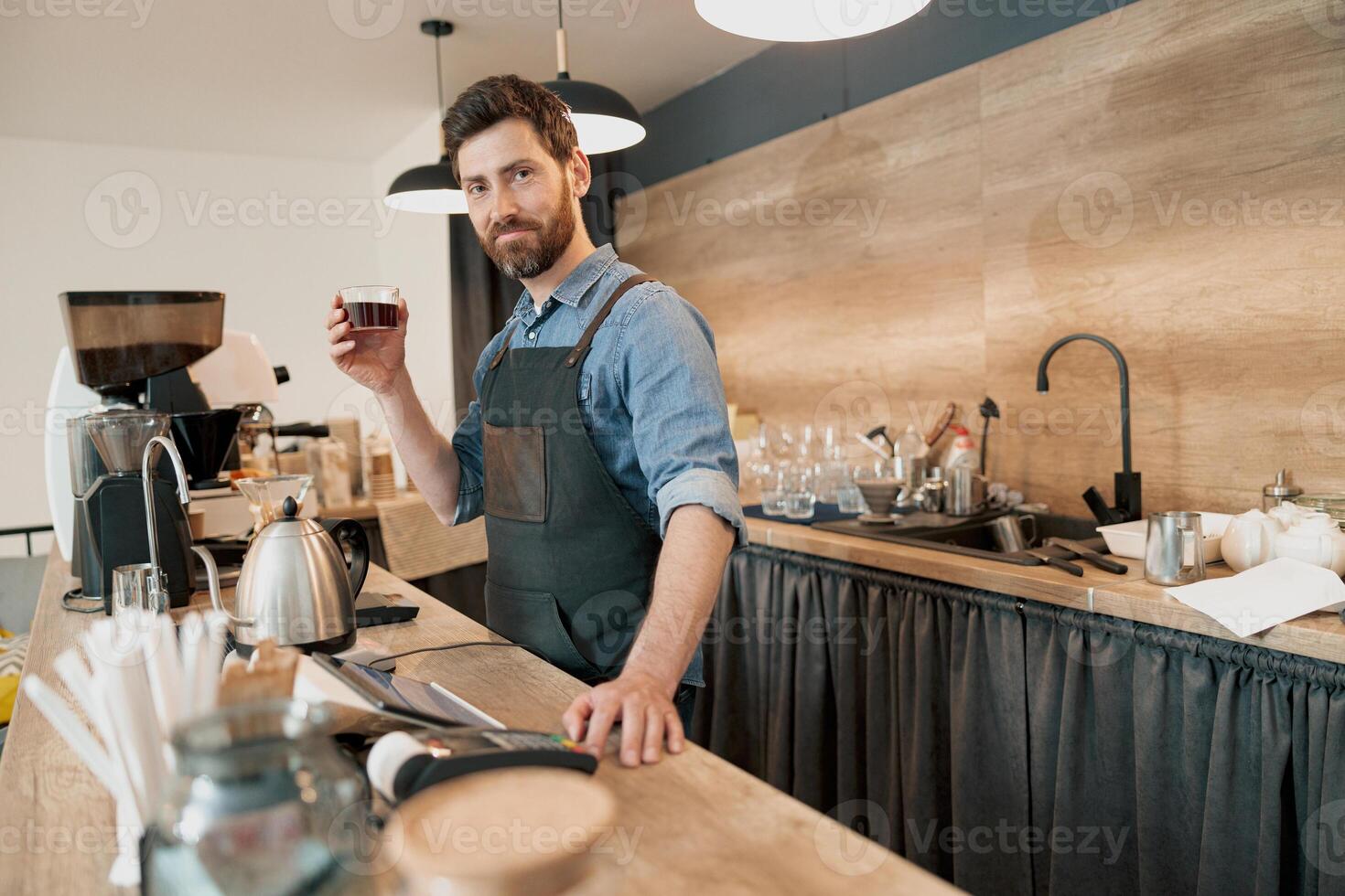 Smiling barista holding in hand glass with filter coffee and looking at the camera photo
