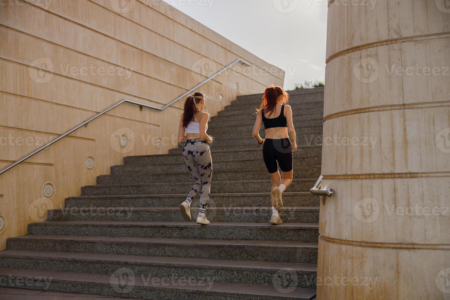 Back view of active female friends in sportswear running on steps outdoors on a sunny day photo