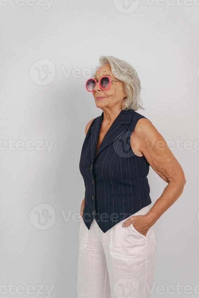 A stylish senior woman wears a vintage vest and trendy sunglasses, exuding confidence photo
