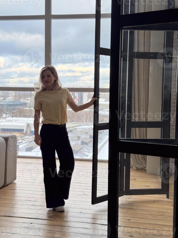 Blond woman in black outfit posing on terrace. Portrait of happy girl i smiling and resting on balcony. photo