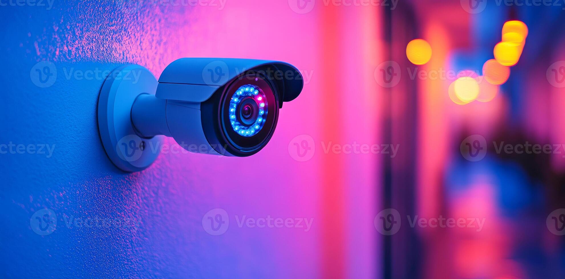 Colorful night security cam. A security camera is mounted on a wall, illuminated by vibrant blue and pink lights in a dimly lit corridor. photo