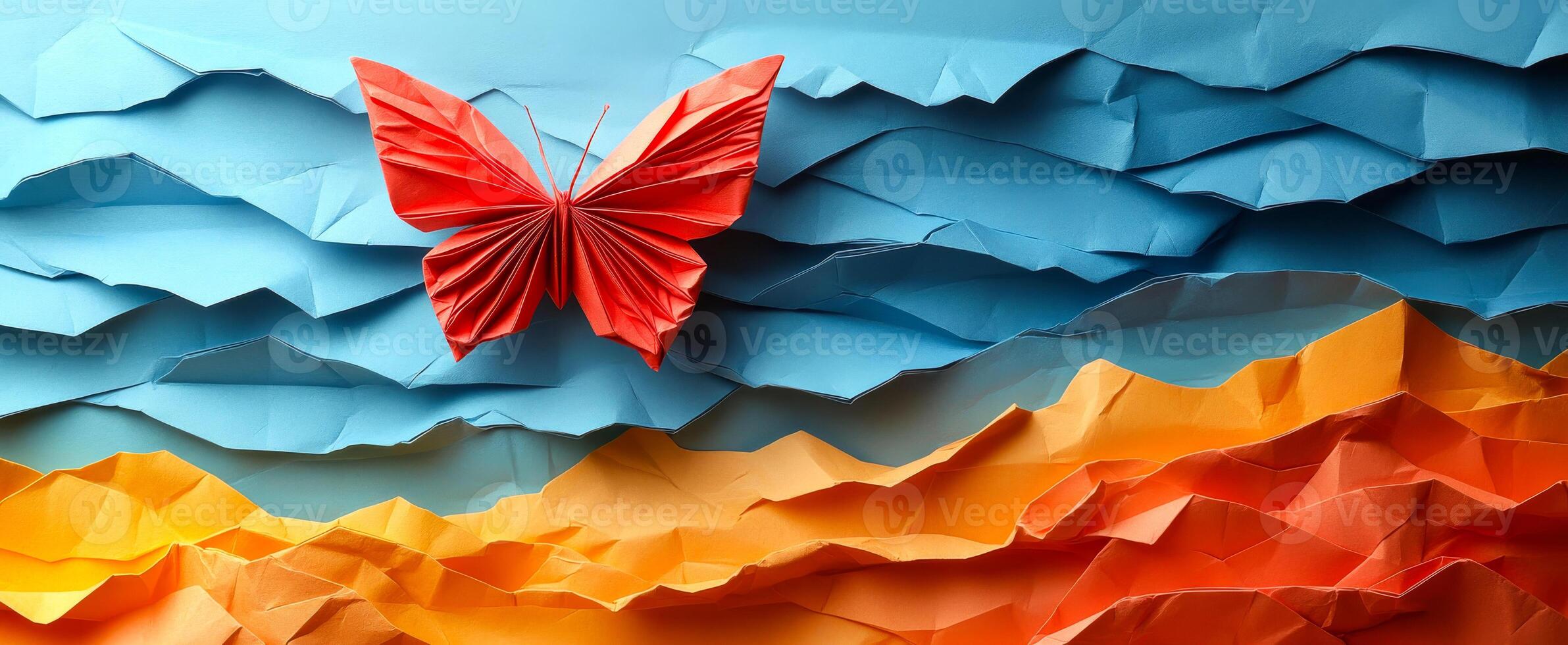 Colorful butterfly on a landscape. A vibrant red butterfly crafted from paper hovers above a textured, multicolored landscape of blue and orange hues. photo