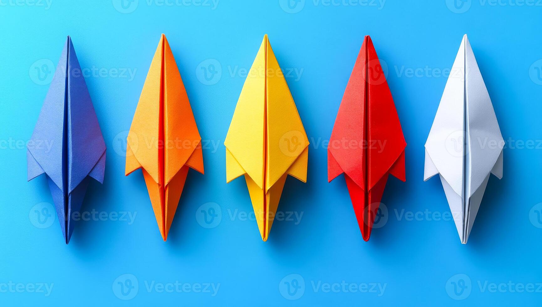 Colorful paper planes arranged in a row. Five colorful paper planes are lined up against a blue background, showcasing playfulness and creativity. photo