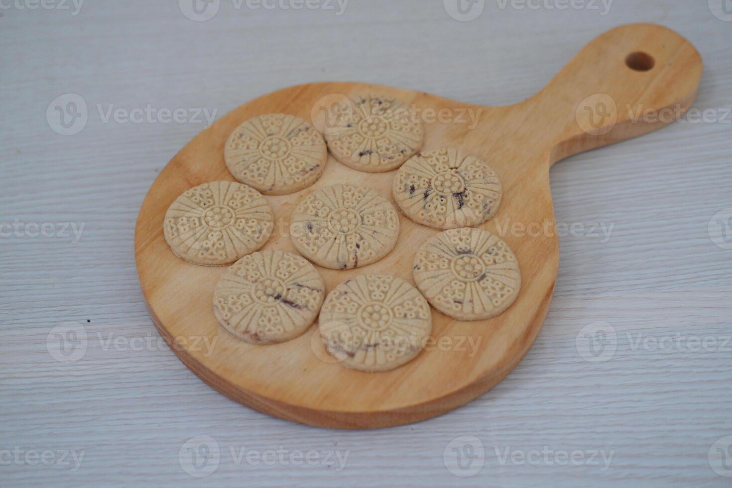 nine round cookies neatly arranged on a small wooden serving board with a handle photo