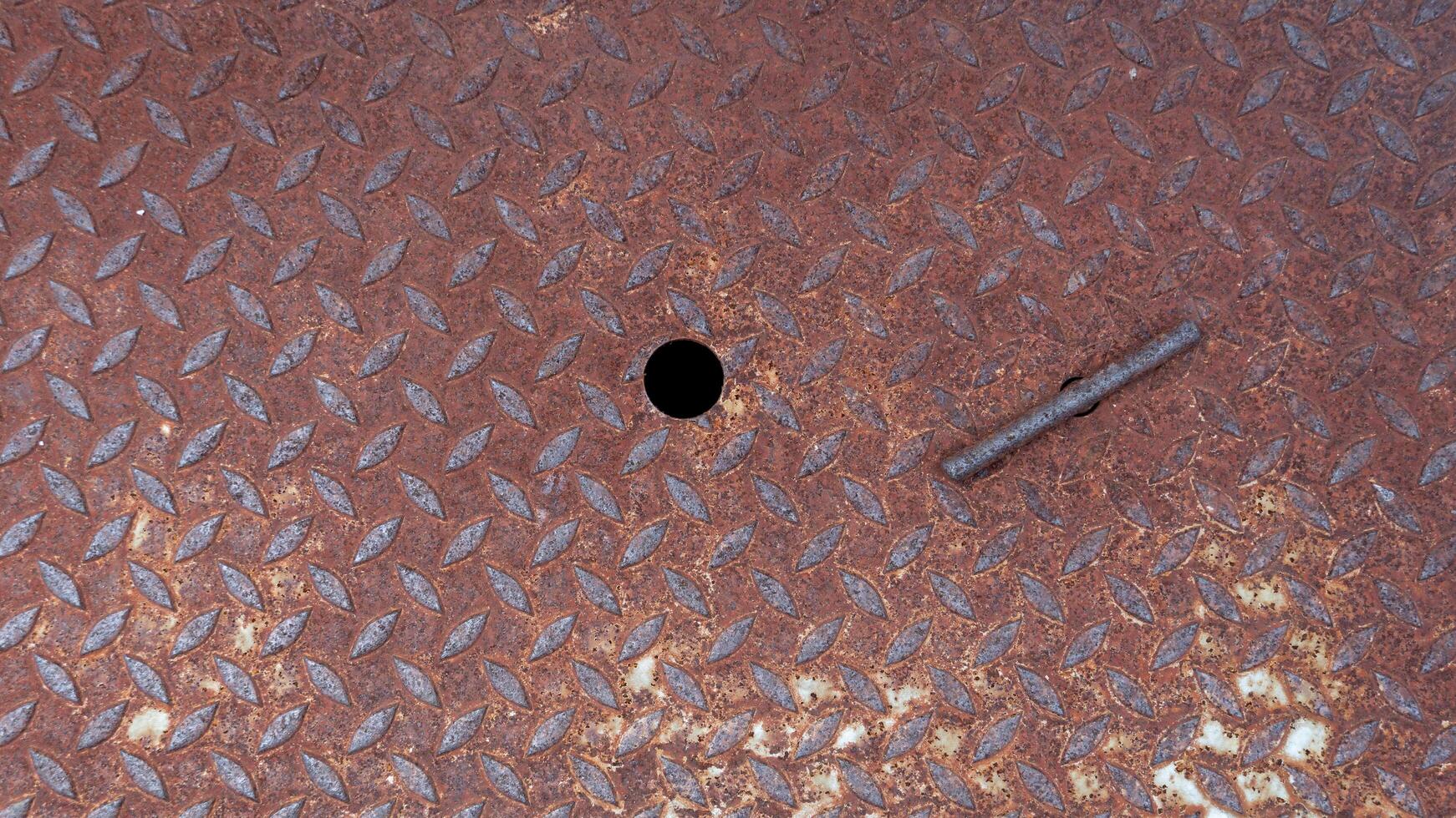 Close up of a rusty metal Lid plate. Raised textured pattern of Lid provides a non slip surface. See the steel rods for pulling the pipe and the ventilation holes. photo