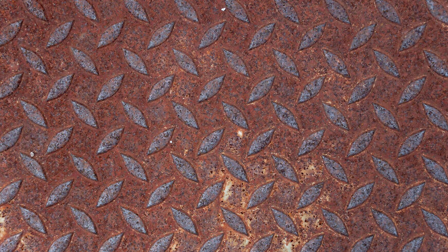 Close up of a rusty metal Lid plate. Raised textured pattern of Lid provides a non slip surface. Overall color is reddish brown due to significant rust formation typical of aged met. photo