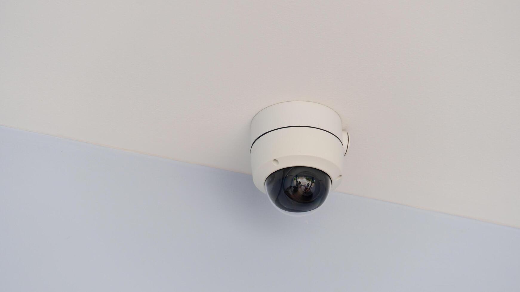 Indoor dome CCTV camera. Inside glass with blurred of activity front of house. Installed under white ceiling panels. photo