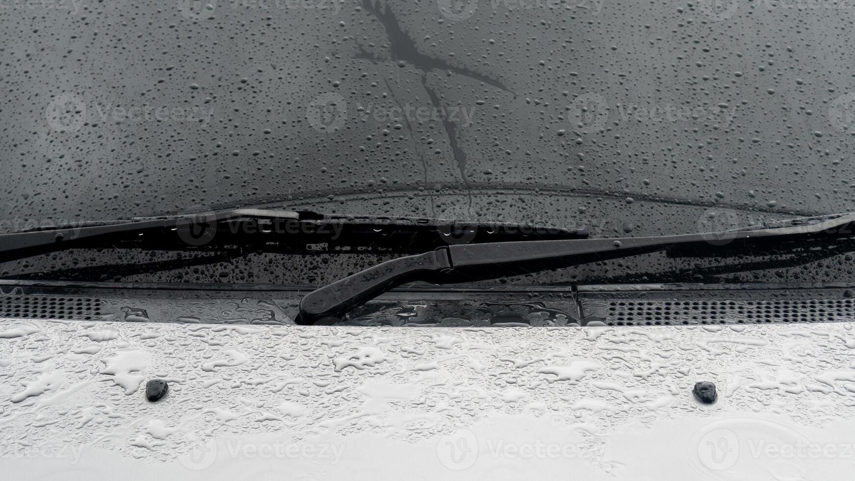 Car gray color covered with raindrops. Focus on two old black wiper blades. Background of car windshield with raindrops flowing down. photo