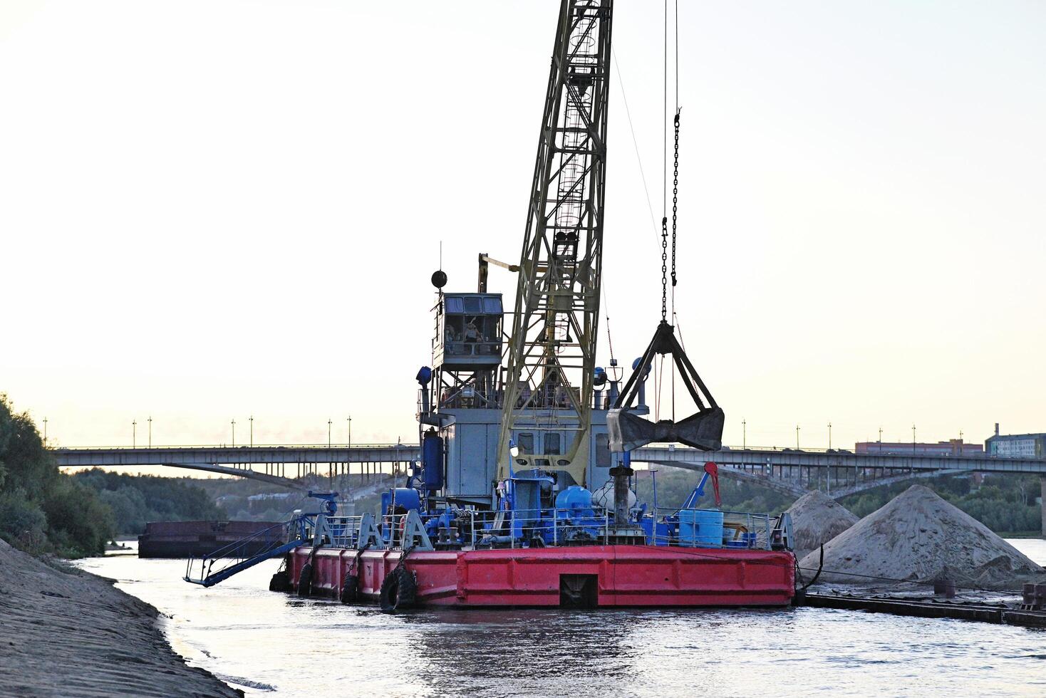 Port cranes on the river bank. Extraction and transportation of sand and other goods. The embankment of the river port, a barge at the mooring wall. photo