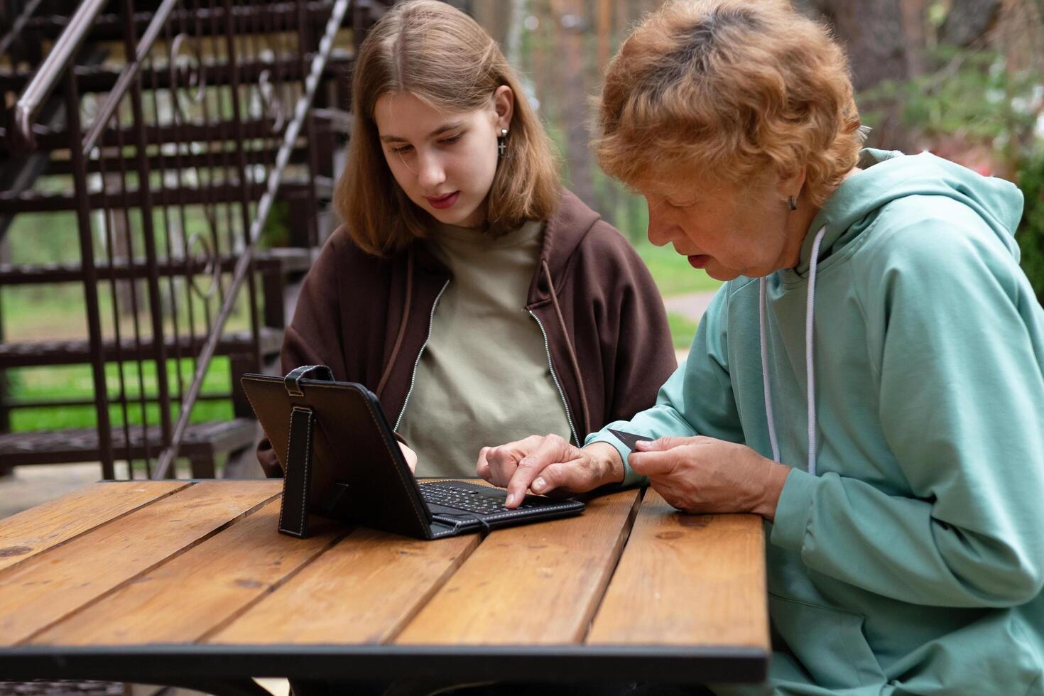 happy teenage girl teaches older 70s grandmothers to use a laptop at home. social media and modern technologies a pensioner studies in online security. photo