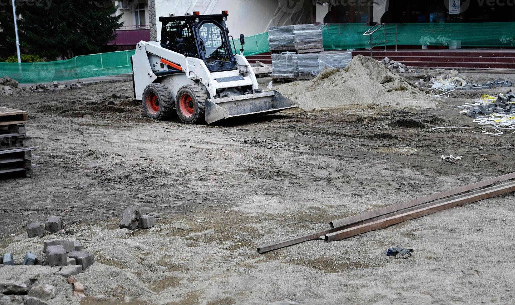 A small tractor works in the sand, filling up a hole. Shovels are on the ground. View from above. photo
