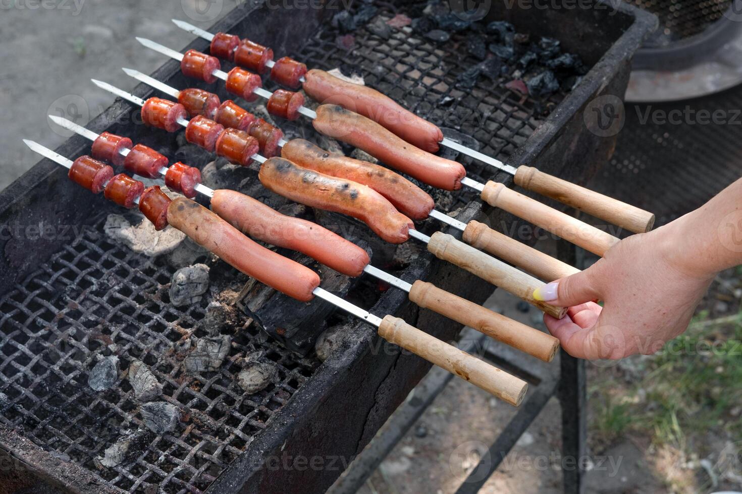 female hand frying sausages on skewers on grill. photo