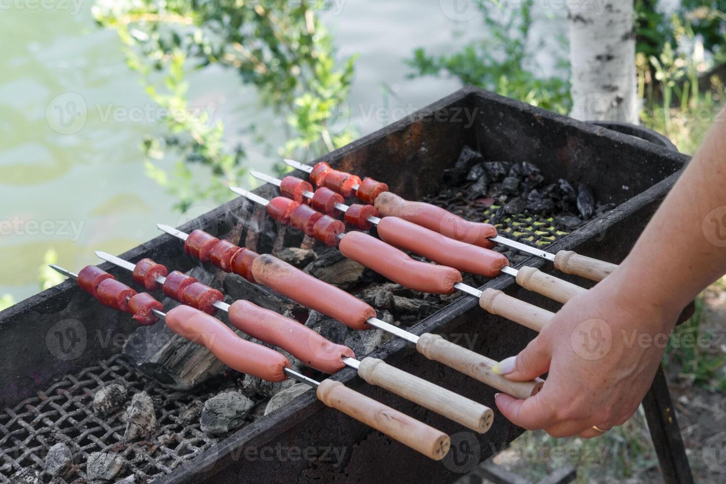 hand frying sausages on skewers on grill. photo