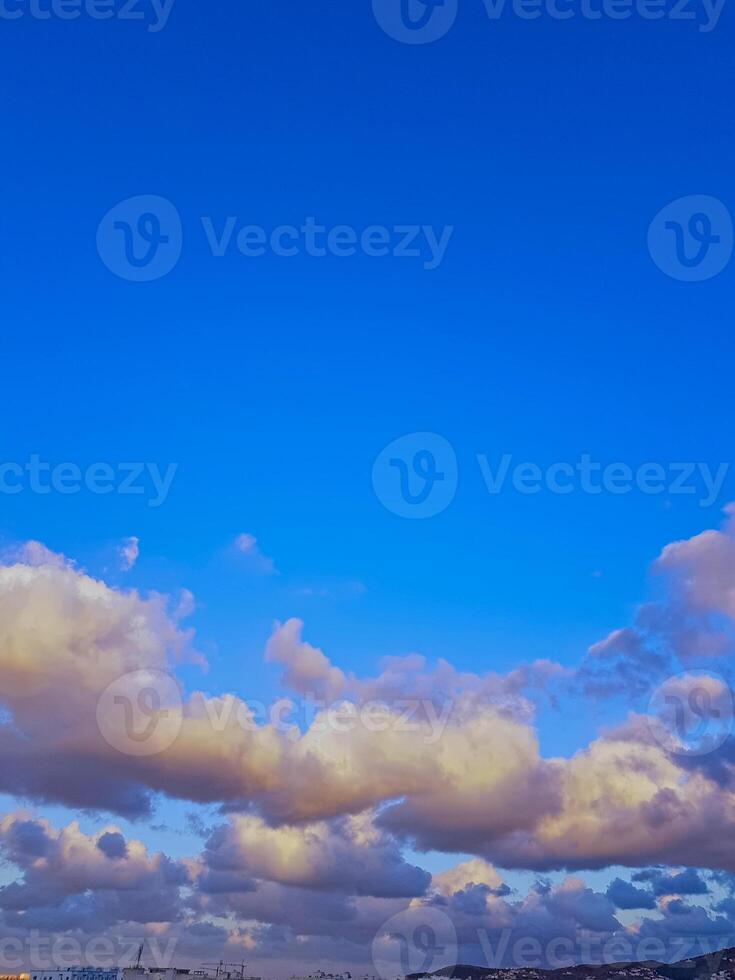 Rugs of rugged clouds drift across the upper half of the horizon, casting a soft glow on the urban scene and natural beauty, while the front sky remains clear and blue. photo