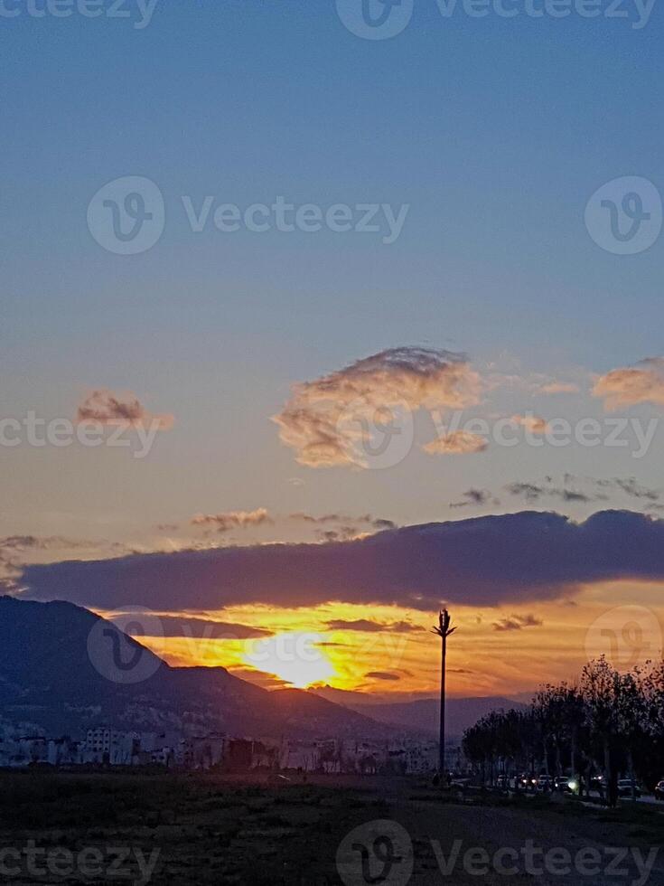 As the sun sets, a breathtakingly picturesque scene unfolds, bathing the landscape in a warm, golden light that emanates from the horizon, nestled between rugs of clouds. photo