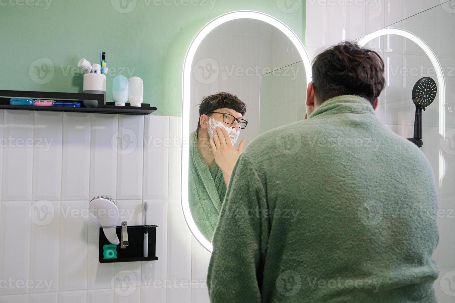 man Shaving with Electric Razor in front of a Mirror photo