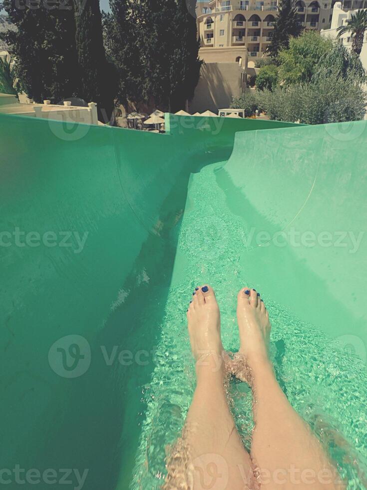 A person with painted toenails slides down a green water slide photo