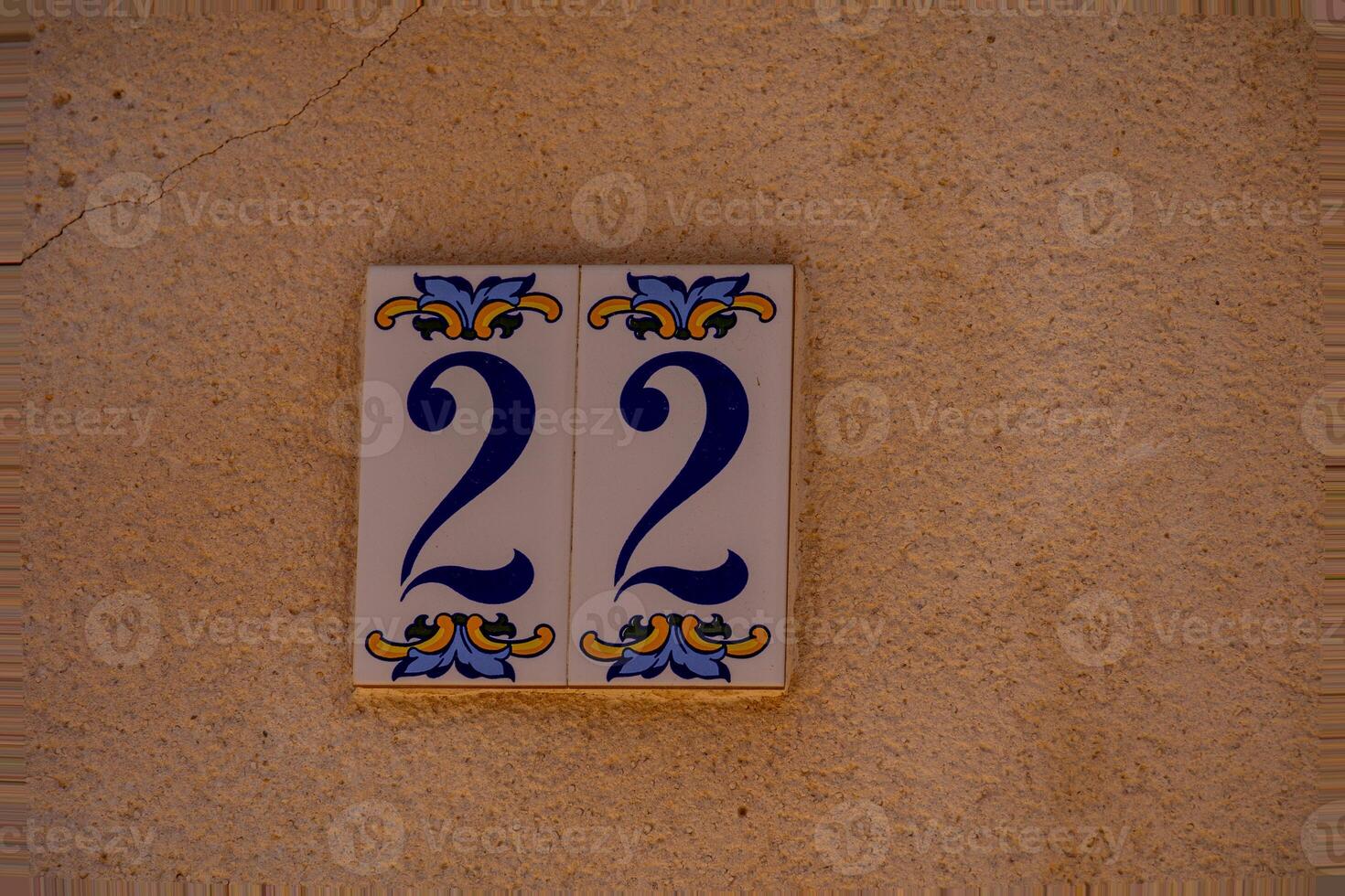 A ceramic tile with the number 22 is mounted on a textured, reddish-brown wall. photo