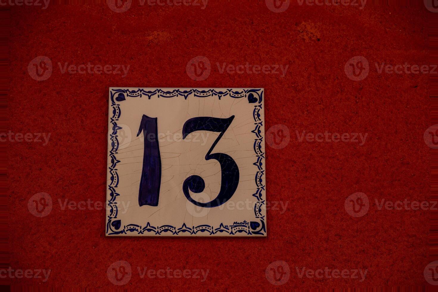 A ceramic tile with the number 13 is mounted on a textured, reddish-brown wall. photo