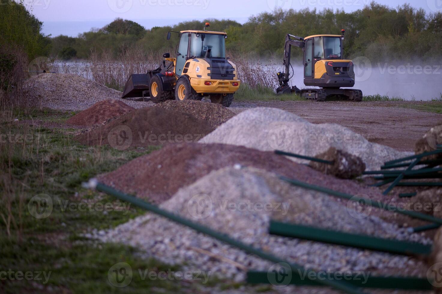 Two tractors and heaps of rubble at dawn by a pond or lake. Fog or mist, nature. photo