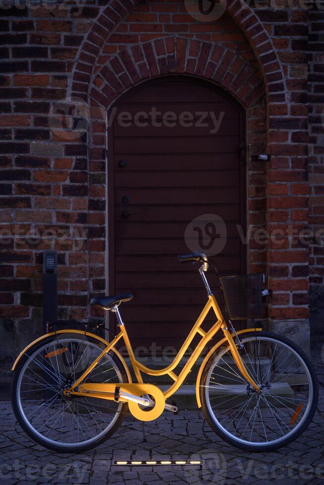 A bright yellow bicycle or bike infront of an old brick wall at night. Sweden photo