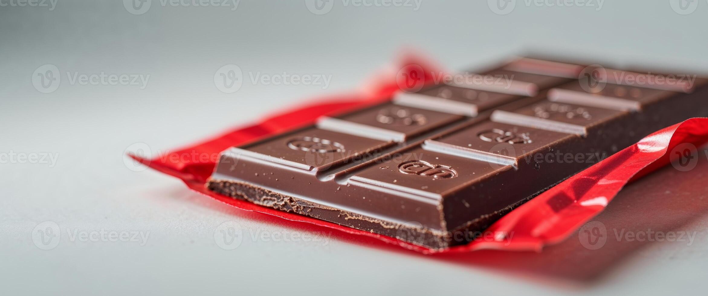 A piece of chocolate is sitting on top of a red wrapper photo