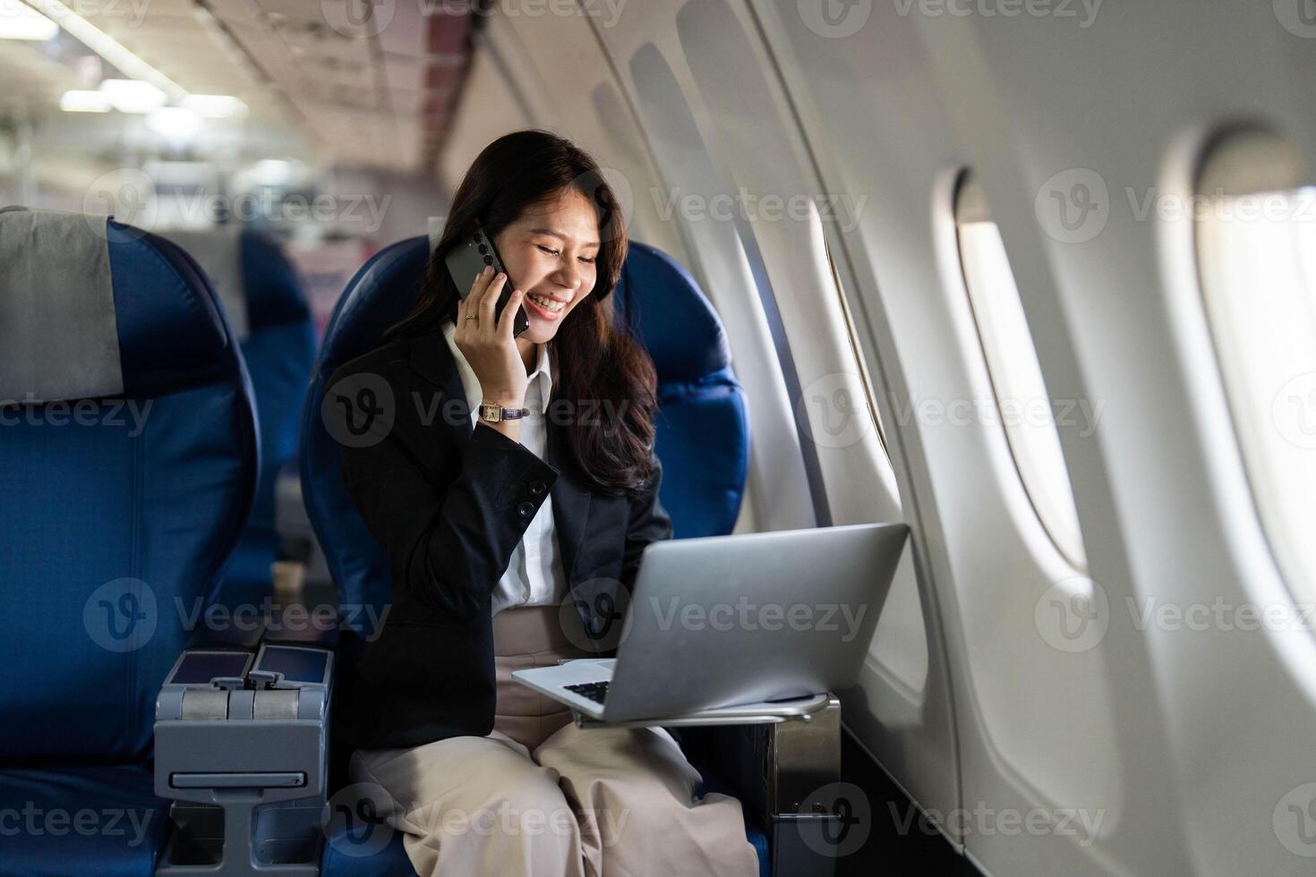 Business travel with a young professional woman working on a laptop and talking on the phone in an airplane photo