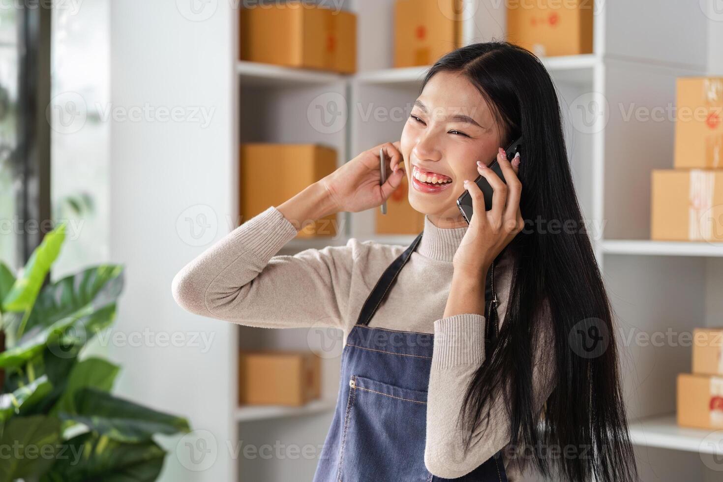 Happy young woman in apron talking on the phone while managing inventory in a modern workspace. photo
