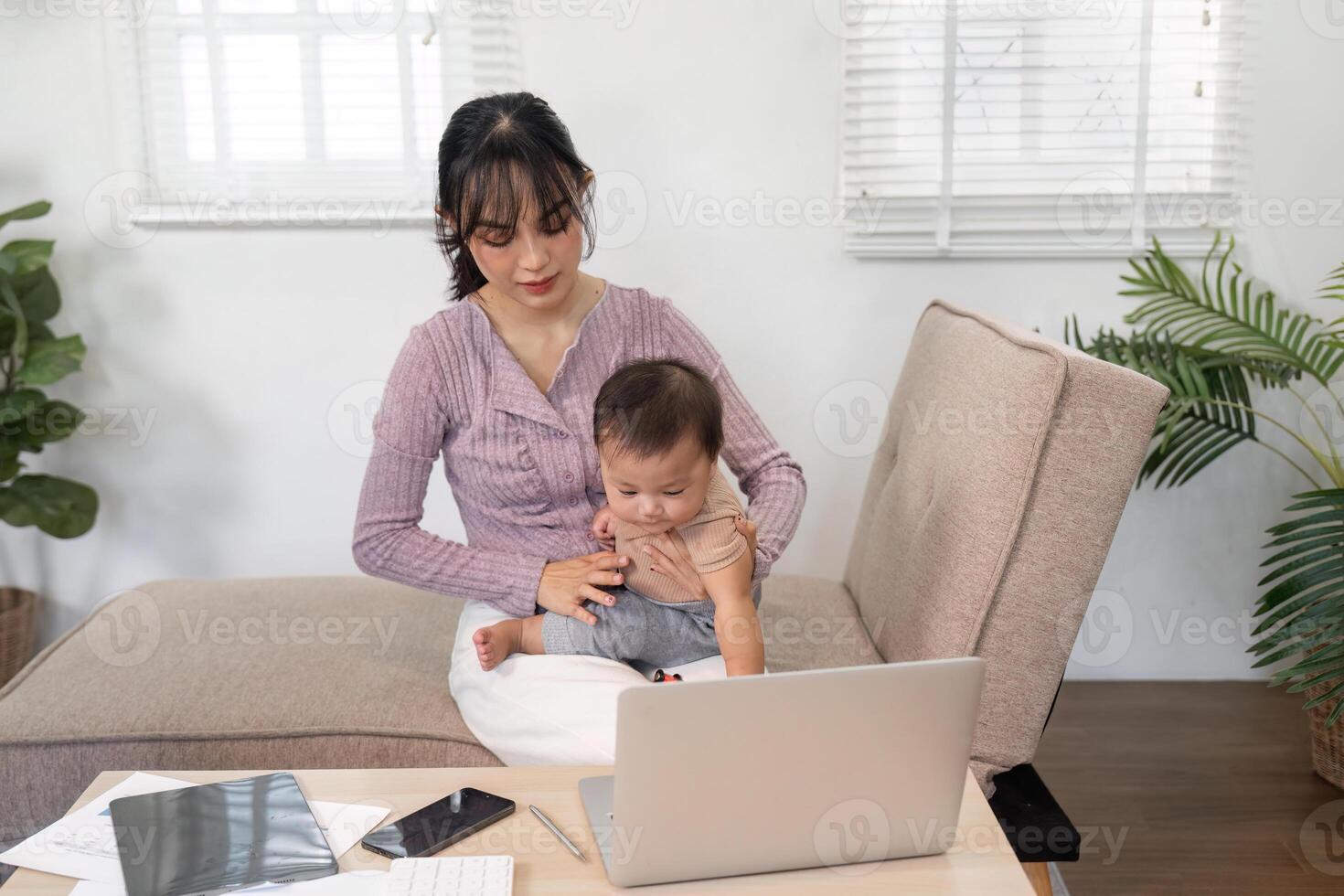 Engaged mother interacting with her baby while working on a laptop at home photo