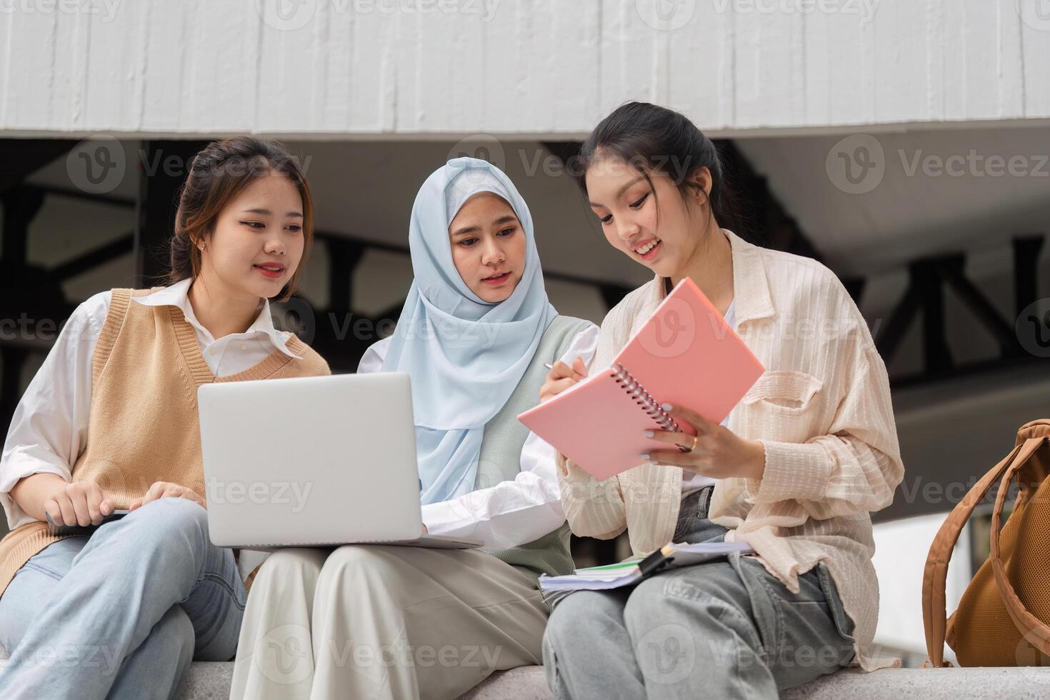 Diverse female students studying together, sharing notes and using a laptop. photo