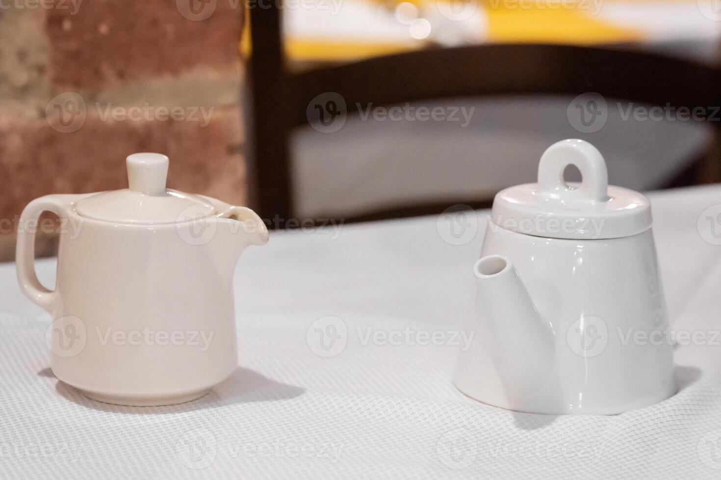 Two teapots on table with brick wall background photo