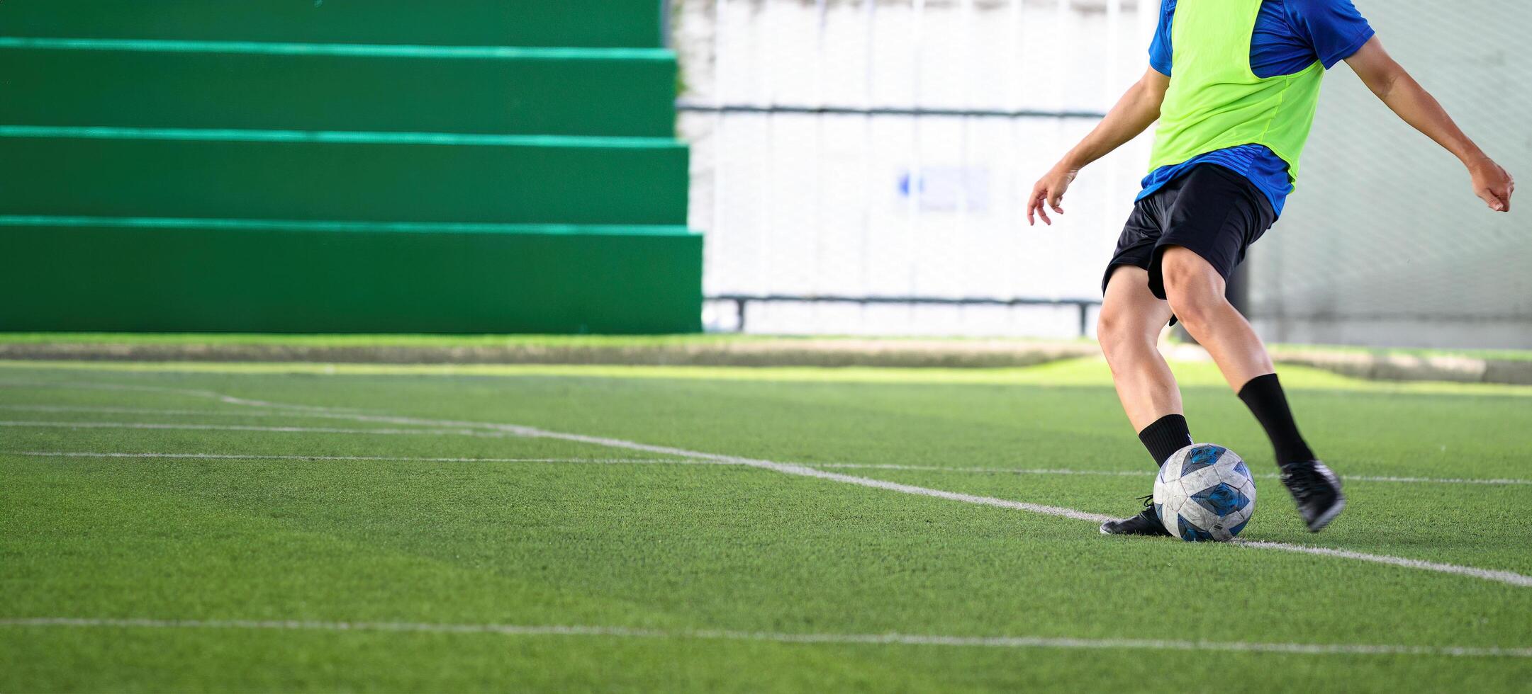 Soccer player in green vest kicking ball on grass field during practice, showing focus and athletic movement in sports environment photo