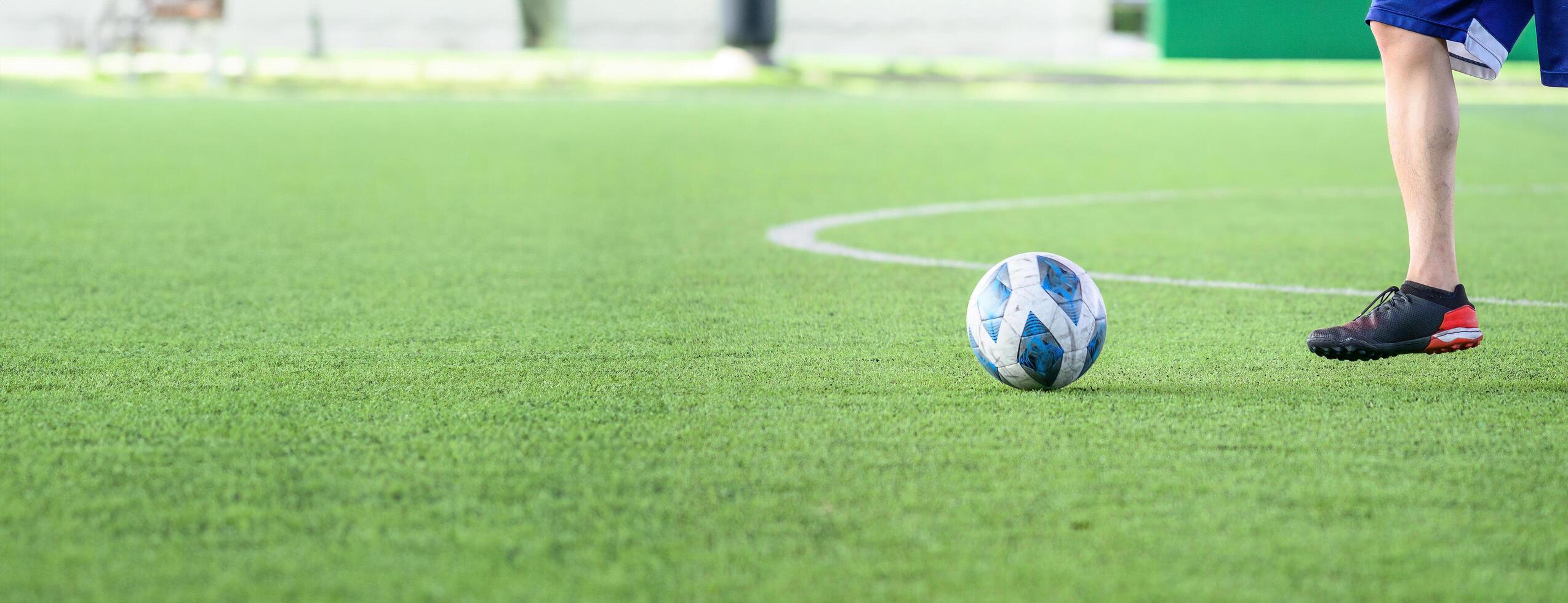 Soccer player wearing black cleats and blue shorts standing on green grass field with white lines near blue and white soccer ball ready to play outdoor game photo
