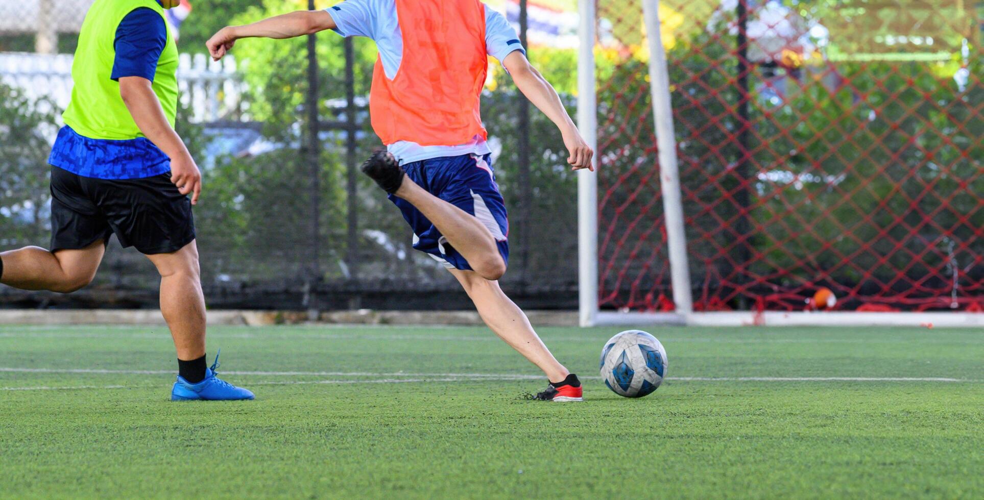Soccer players in action during game on grass field focusing on their legs and ball with vibrant jerseys and goal net in background creating energetic sports scene photo