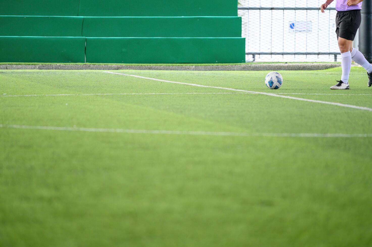 Soccer player on green grass field with white lines preparing to kick ball near green bleachers in bright daylight photo
