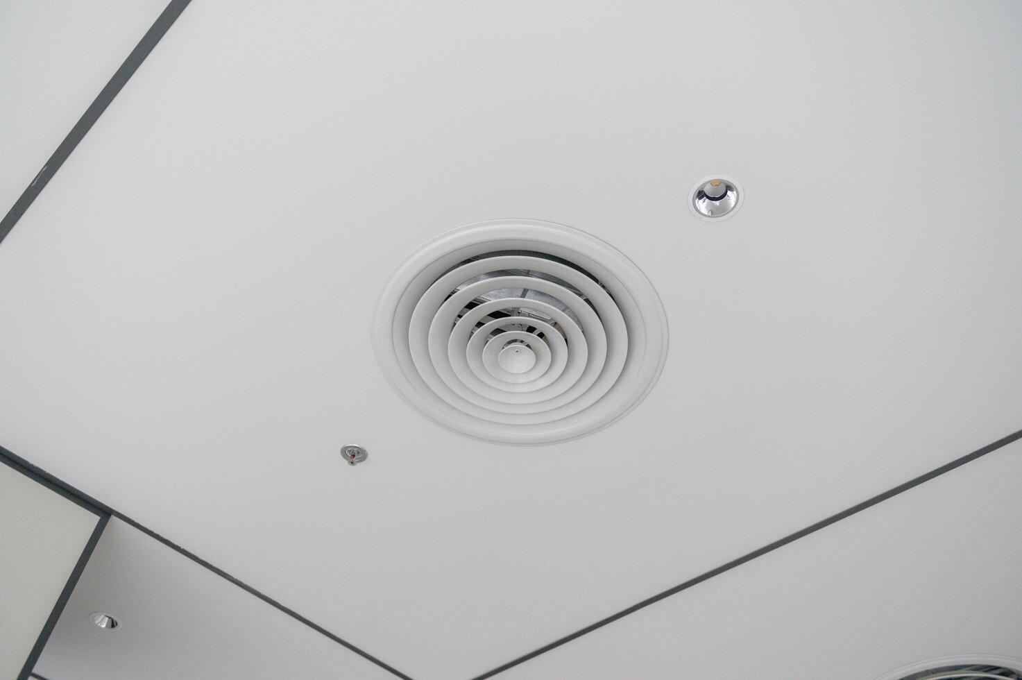 Clean modern office ceiling featuring circular air vent, recessed lighting, and grid pattern with white panels and dark trim creating sleek and functional design photo