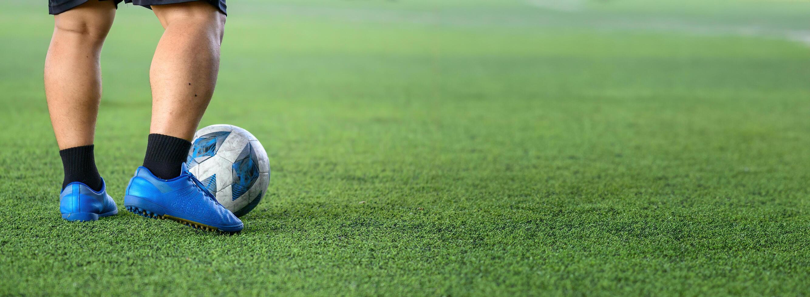 Soccer player standing on green grass field with blue cleats and black socks, focusing on ball near feet during game or practice session photo