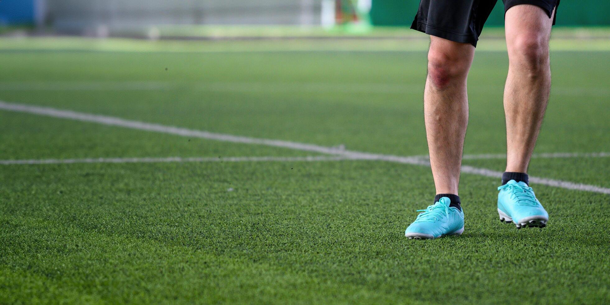 Soccer player standing on green grass field wearing blue cleats and black shorts ready for action in sports game with focus on legs and shoes photo