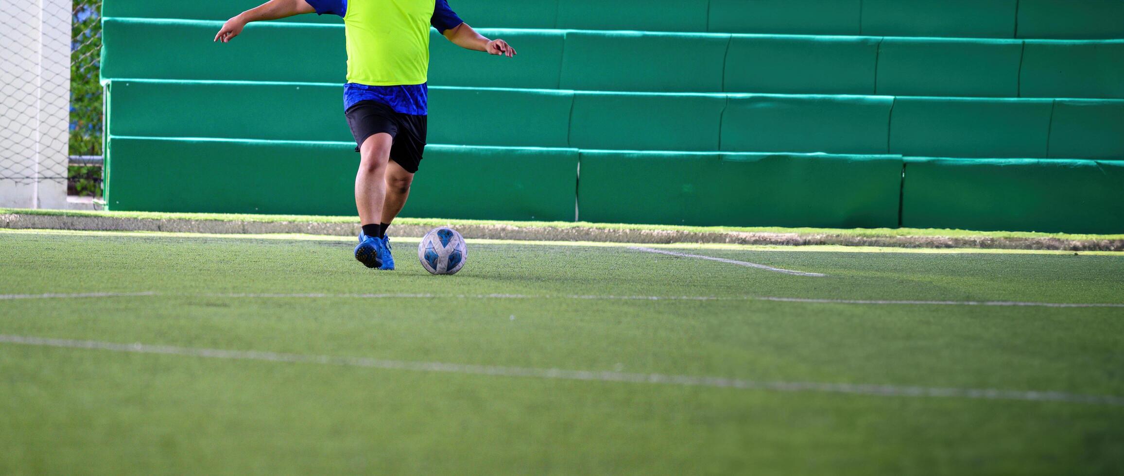 Soccer player in bright yellow jersey kicking ball on green artificial turf field during practice session with green padded wall in background photo