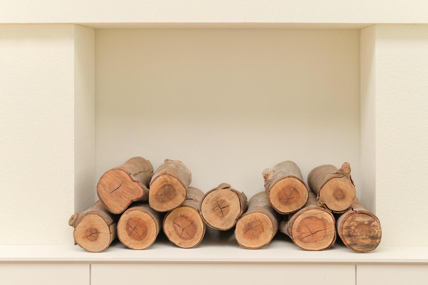 Stacked firewood logs neatly arranged in cozy interior space with clean white shelf and light colored wall creating warm atmosphere photo