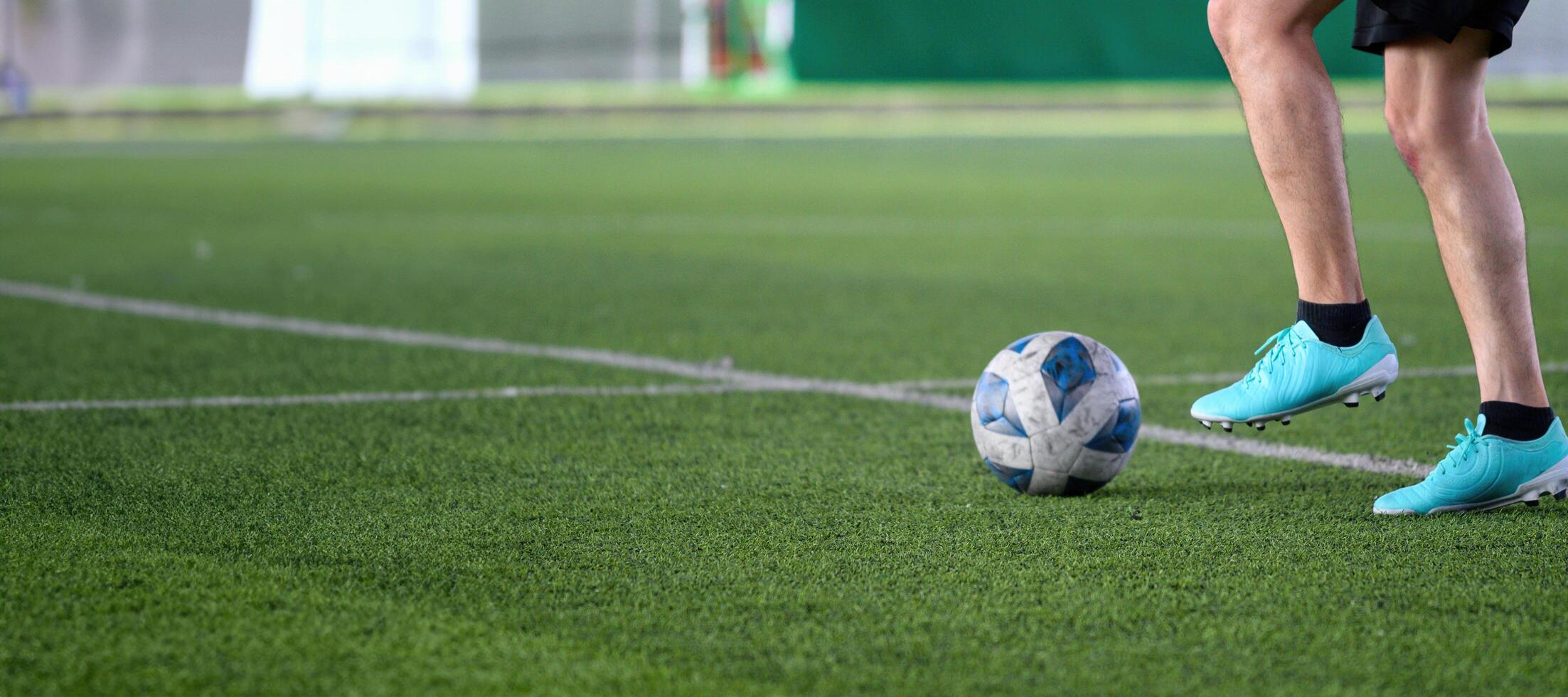 Soccer player wearing blue cleats controlling ball on green grass field during game, focusing on legs and ball with white field lines visible in background photo