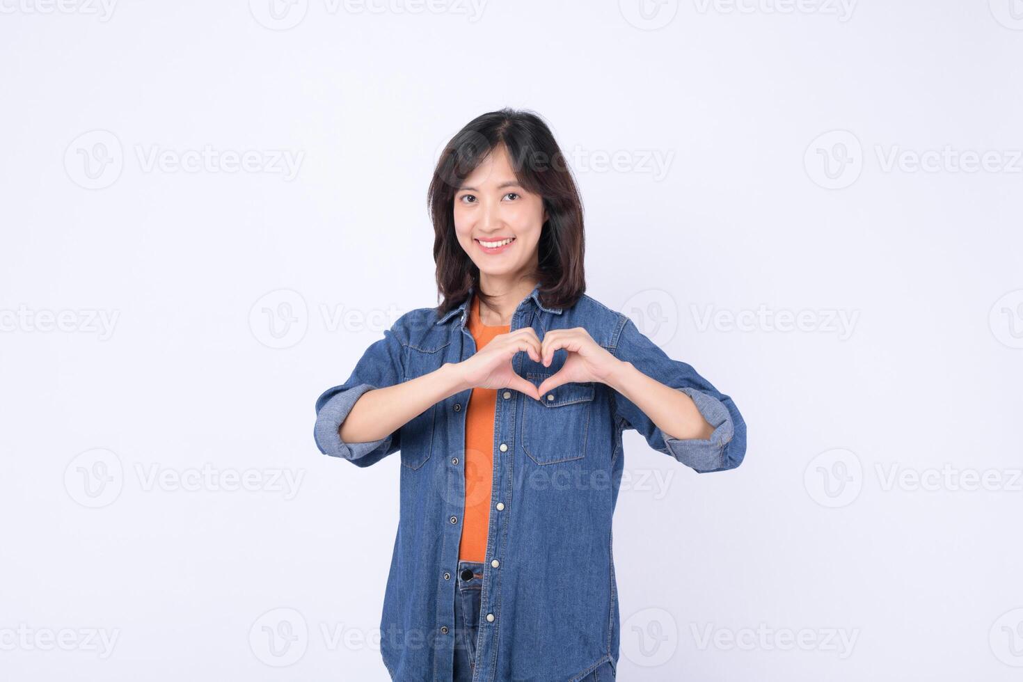 Southeast asian woman smiling warmly and making heart shape with her hands for advertising positive message of love and kindness photo