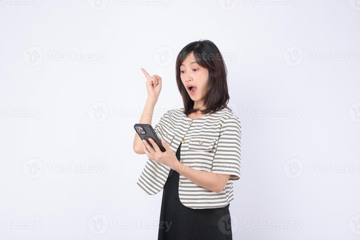 Southeast asian woman looks surprised while using mobile phone to access internet application showing excitement and discovery in bright studio setting photo